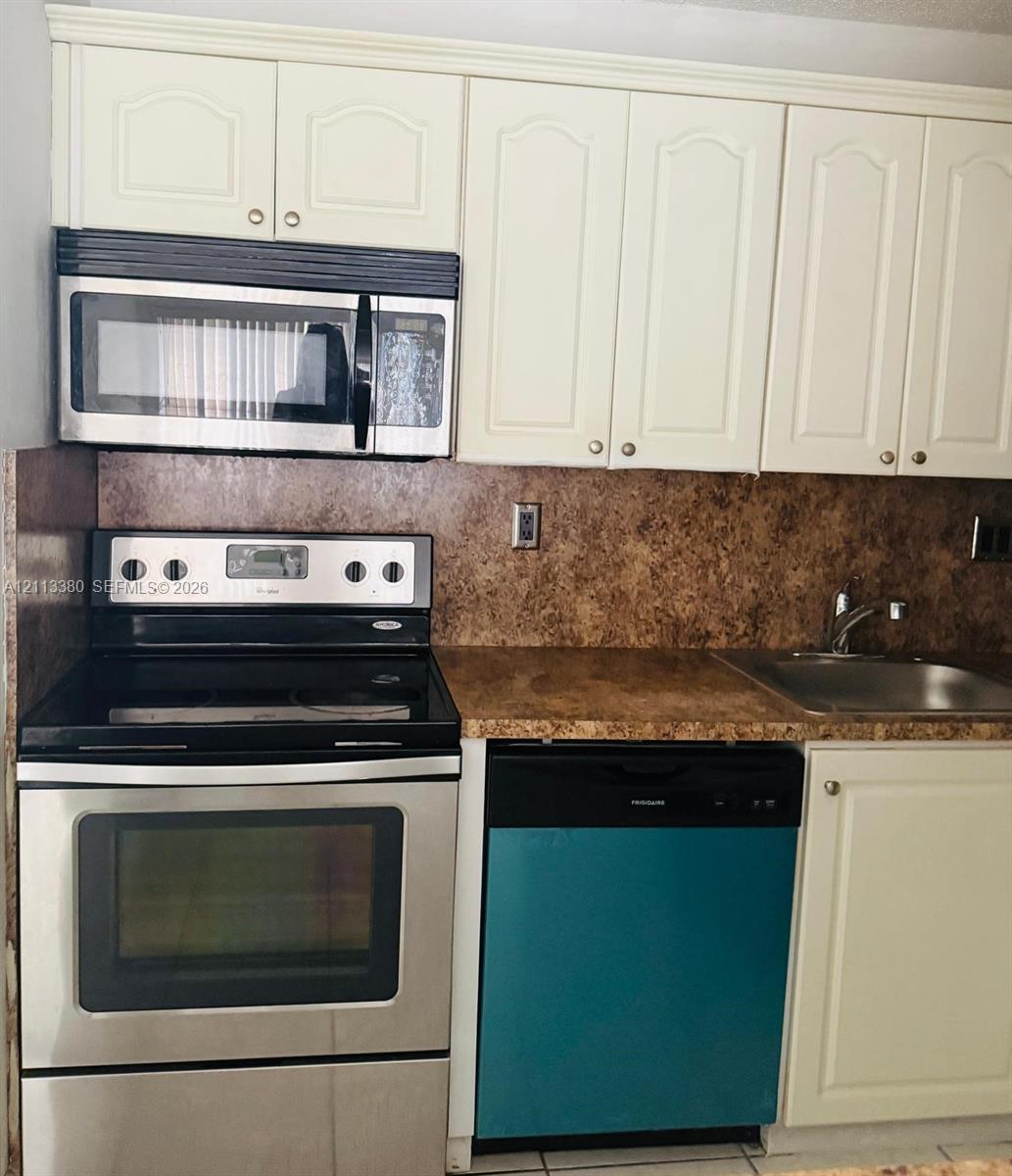 Kitchen featuring off-white raised-panel cabinetry, stone-finish countertops, stainless steel electric range, over-the-range microwave, and stainless steel undermount sink