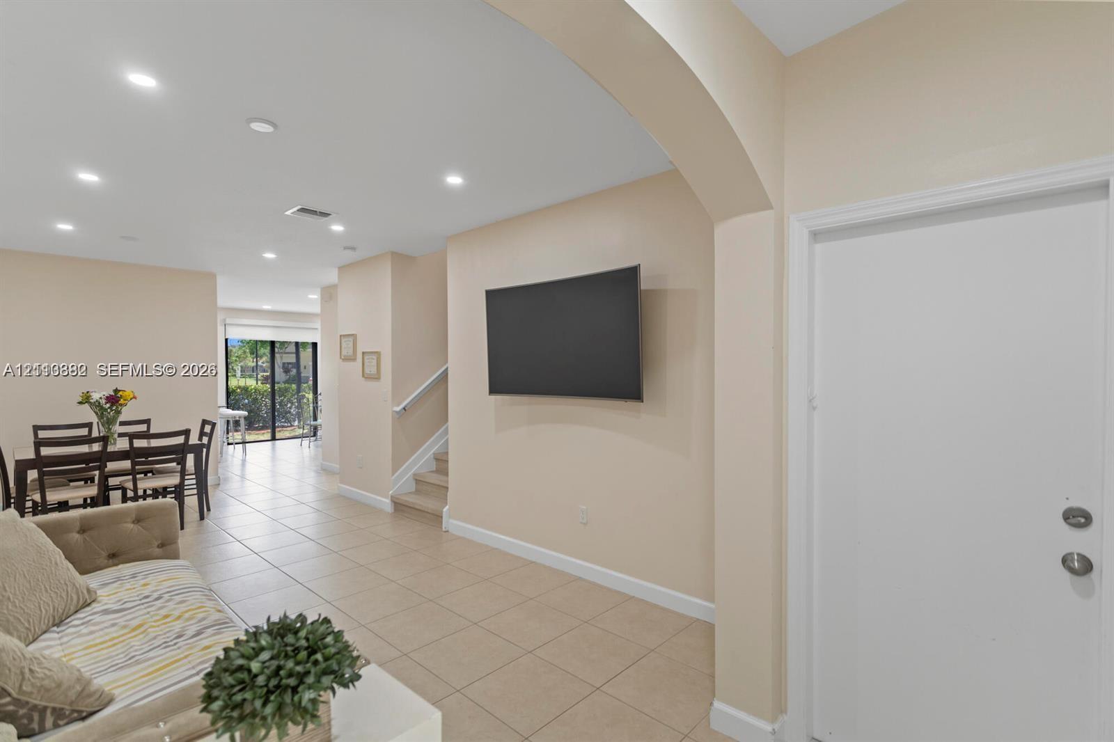 Interior space featuring neutral-toned tile flooring, recessed ceiling lighting, a curved architectural archway, and a staircase with a white handrail