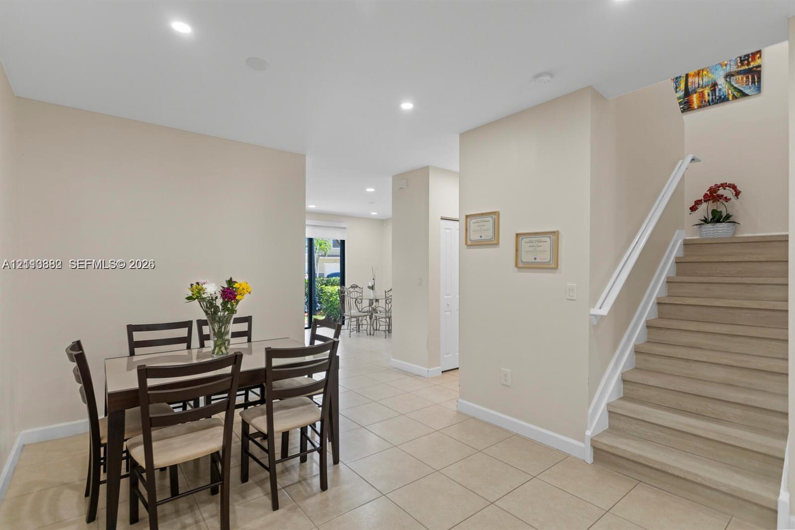 Neutral-toned interior space featuring light-colored tile flooring, recessed ceiling lighting, a staircase with wood-finish treads, and a white handrail