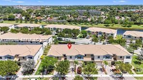 Aerial perspective of a multi-unit residential property featuring a tiled roof, light-toned exterior siding, and paved driveways, situated near a waterway and landscaped green spaces Aerial perspective of a multi-unit residential property featuring a tiled roof, light-toned exterior siding, and paved driveways, situated near a waterway and landscaped green spaces