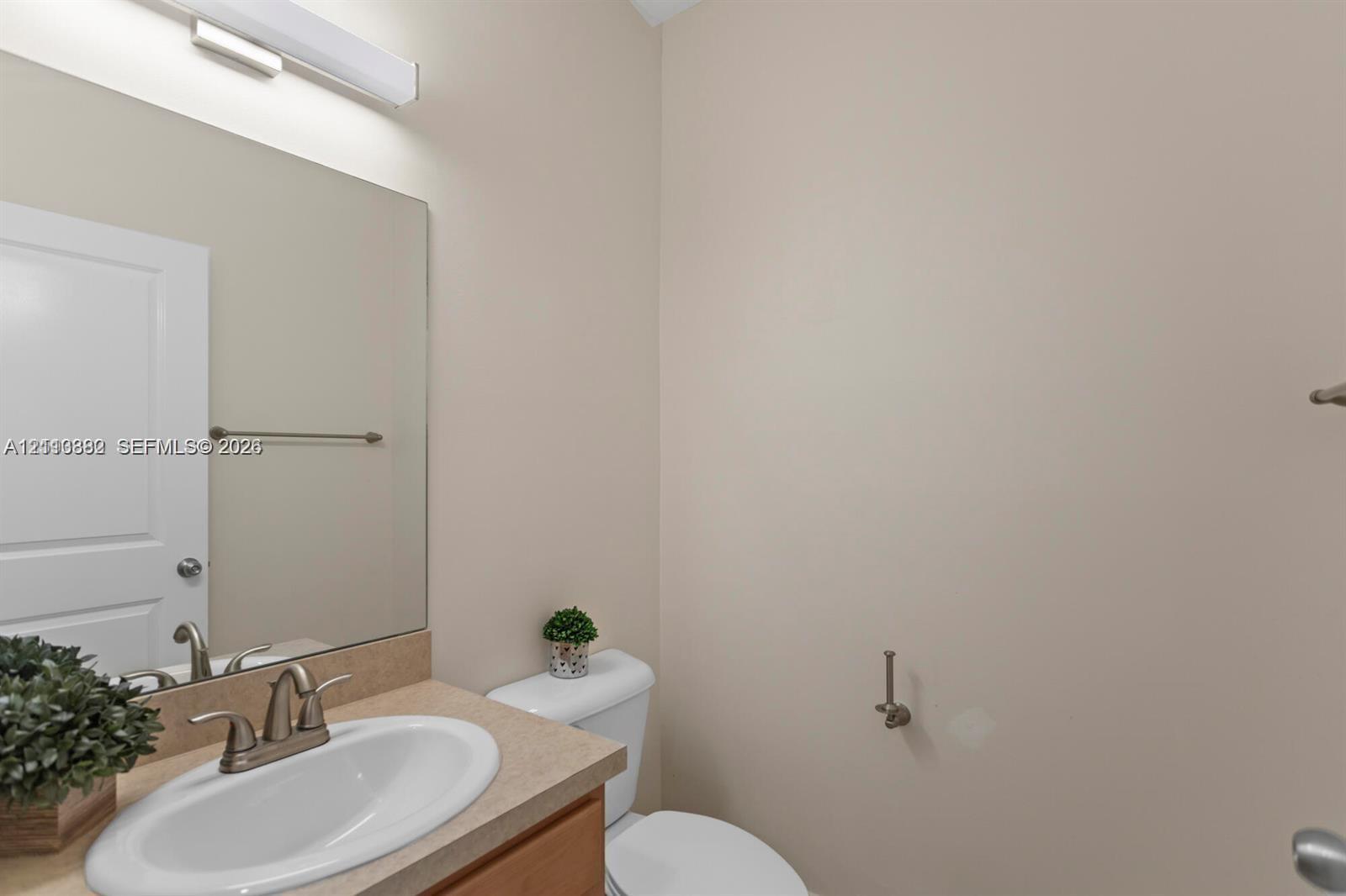 Neutral-toned bathroom featuring a surface-mounted sink, wide vanity mirror, metallic finish fixtures, and a wall-mounted light bar