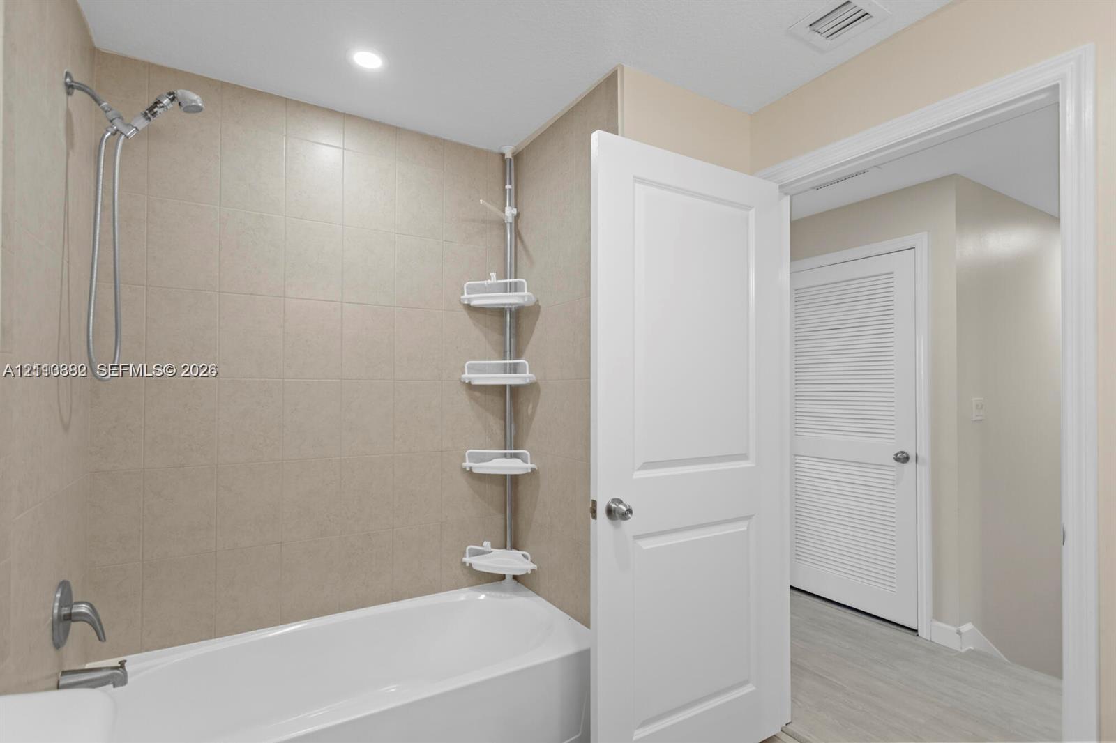 Full-height ceramic tile tub surround with integrated metallic faucet hardware and a recessed ceiling light