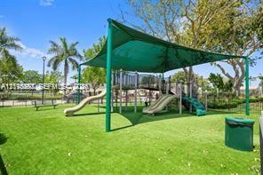 Outdoor recreational area featuring a playground structure with dual slides, protective shade canopy, synthetic turf surfacing, and surrounding mature trees Outdoor recreational area featuring a playground structure with dual slides, protective shade canopy, synthetic turf surfacing, and surrounding mature trees
