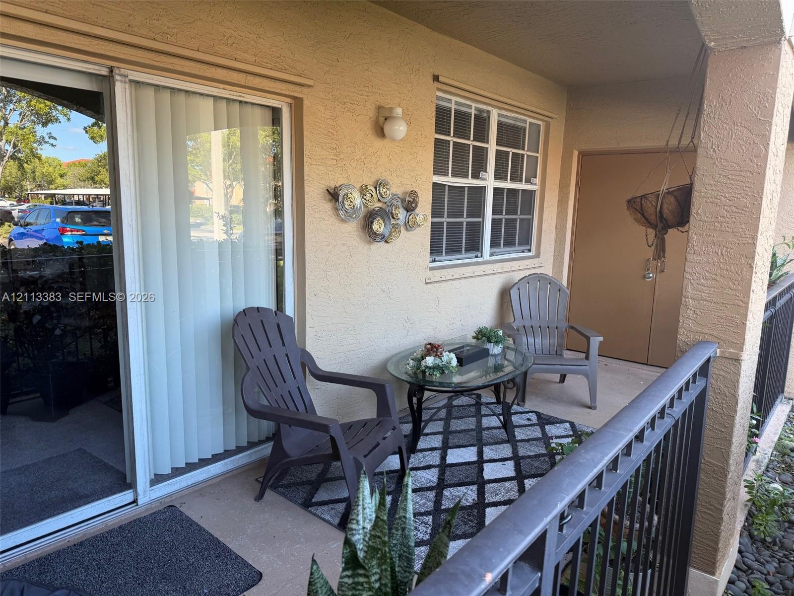 Covered patio featuring concrete flooring, sliding glass door, multi-pane window, exterior wall-mounted light fixture, and metal railing