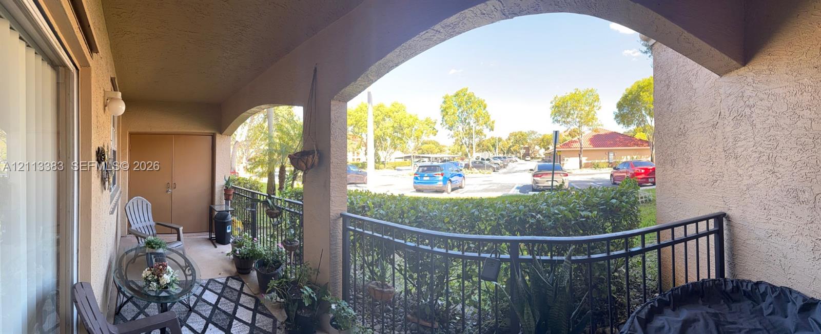Covered patio featuring arched structural supports, metal railings, a textured stucco exterior, and a built-in exterior storage closet