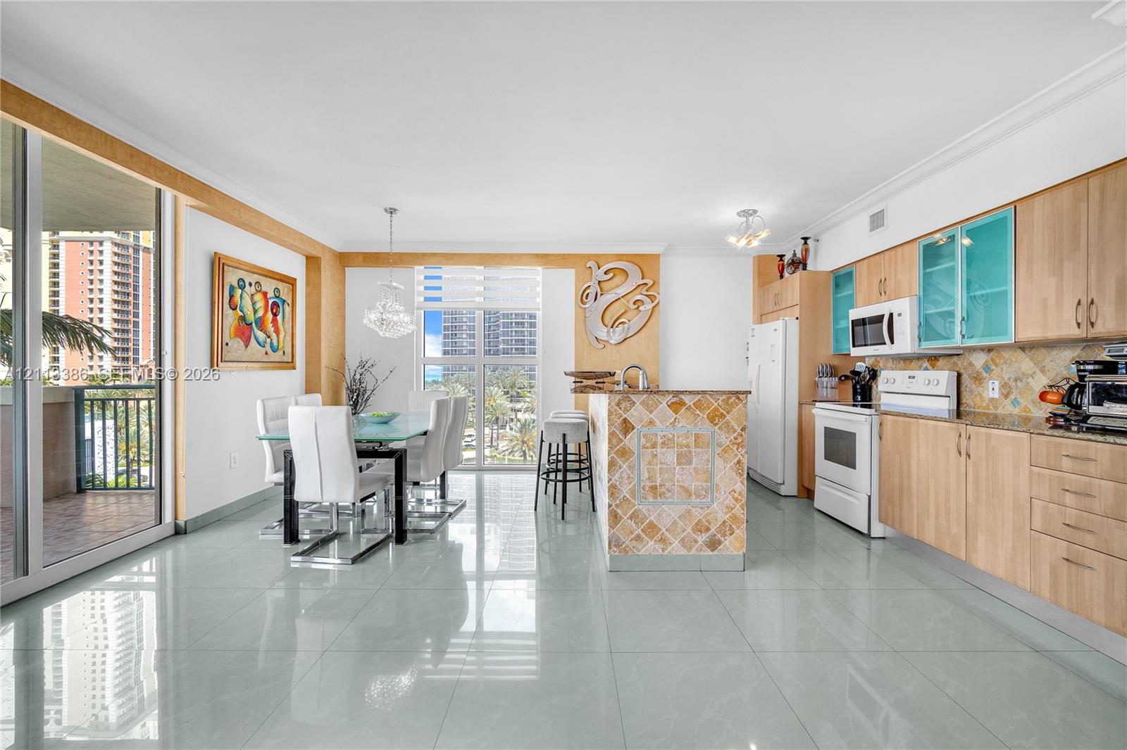 Open-concept area featuring light wood-finish cabinetry, tile-clad kitchen island, polished tile flooring, glass-paneled upper cabinets, and floor-to-ceiling glass sliding doors Open-concept area featuring light wood-finish cabinetry, tile-clad kitchen island, polished tile flooring, glass-paneled upper cabinets, and floor-to-ceiling glass sliding doors