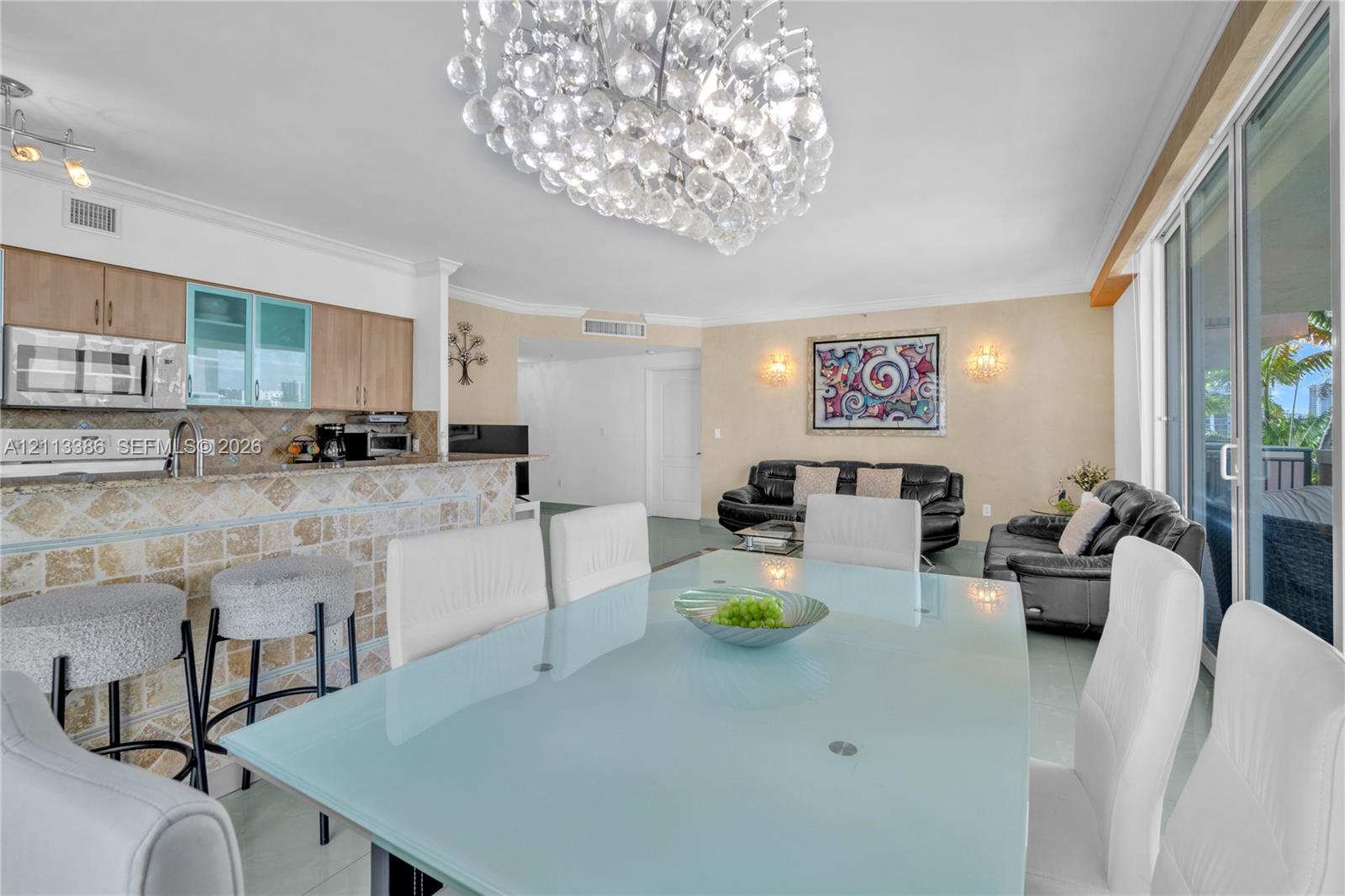 Open-concept living space featuring a tiered tile breakfast bar, glass-front cabinetry, a decorative crystal chandelier, and sliding glass doors