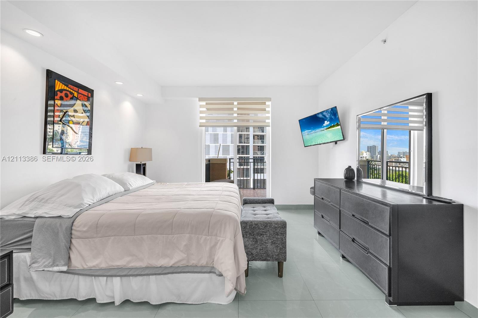 Neutral-toned tile flooring, recessed ceiling lighting, and sliding glass door with integrated window treatments opening to a balcony