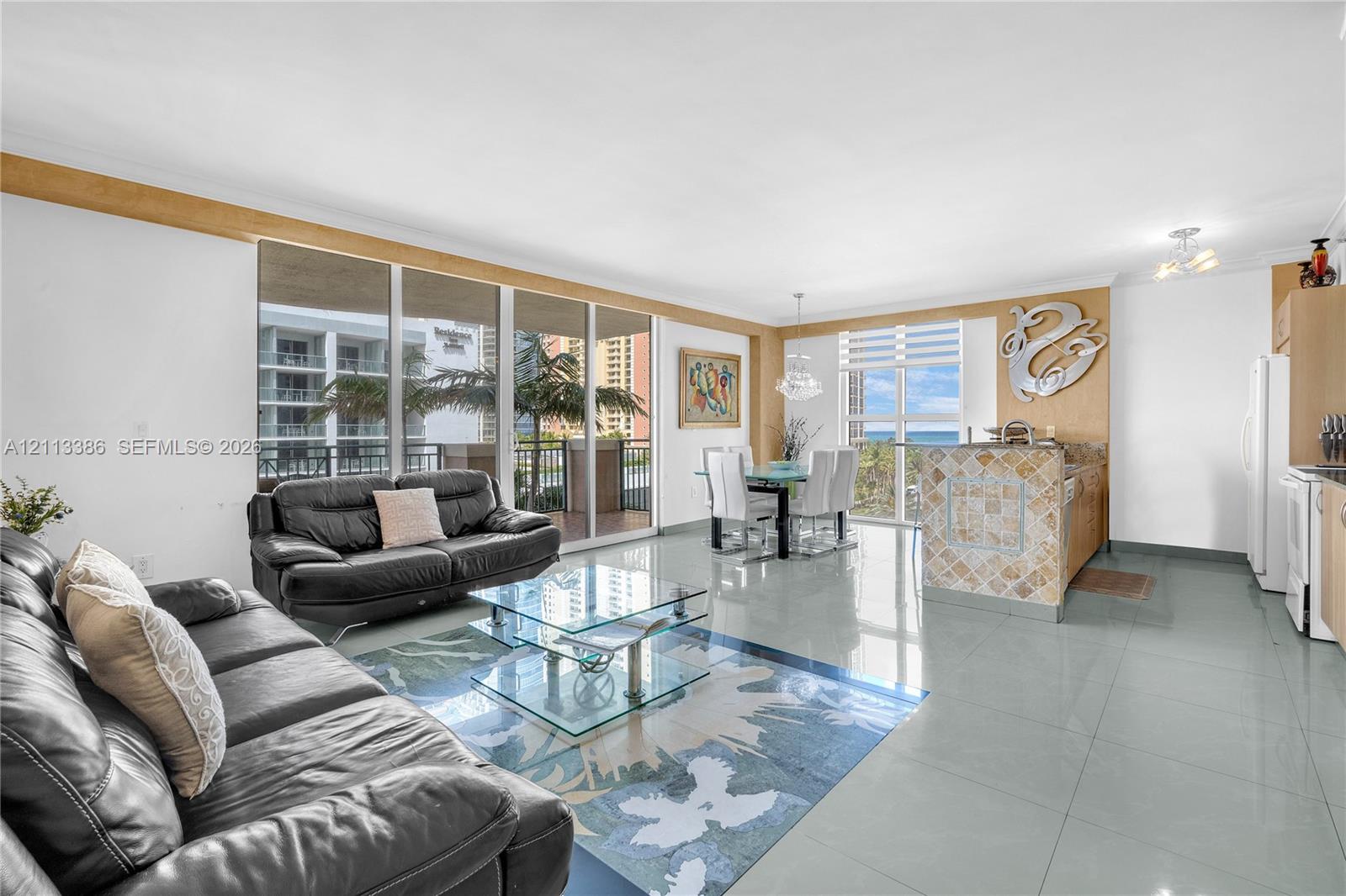 Open-concept living area featuring large-format tile flooring, floor-to-ceiling glass sliding doors, and a kitchen island with stone tile cladding Open-concept living area featuring large-format tile flooring, floor-to-ceiling glass sliding doors, and a kitchen island with stone tile cladding