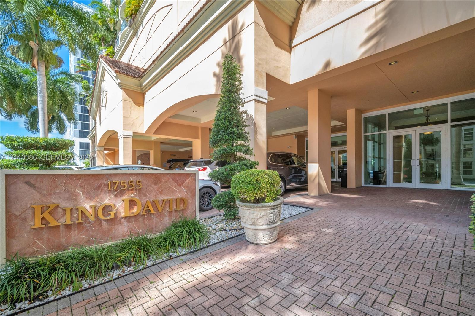 Covered porte-cochre entry featuring a red brick paver driveway, natural stone monument signage, and structured landscape elements Covered porte-cochre entry featuring a red brick paver driveway, natural stone monument signage, and structured landscape elements