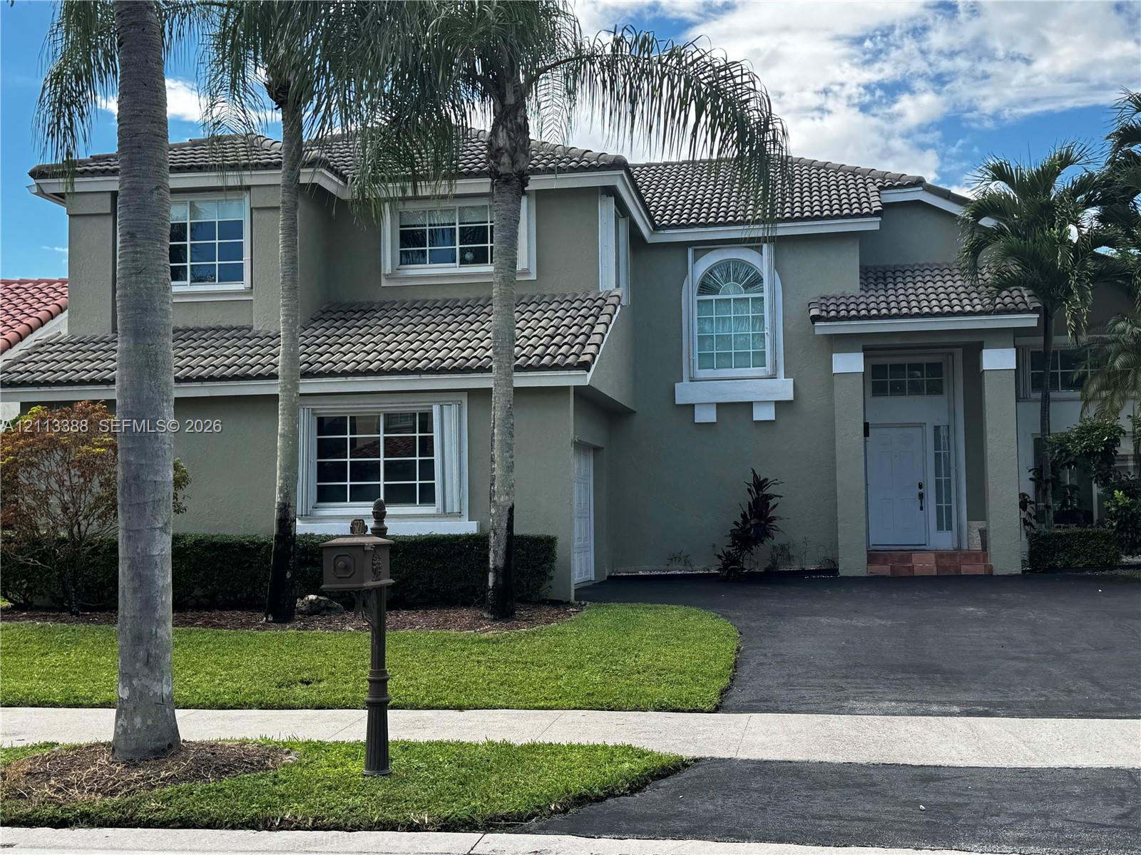 Two-story stucco exterior featuring a multi-gabled tile roof, arched windows, and a paved driveway