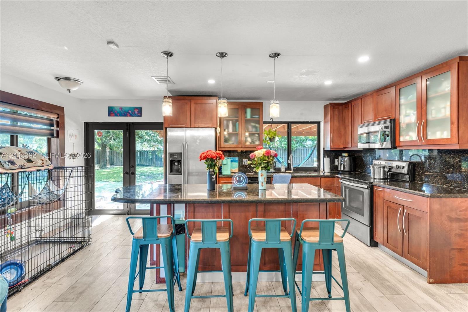 Kitchen featuring wood cabinetry, stone countertops, a center island with pendant lighting, stainless steel appliances, and wood-finish flooring