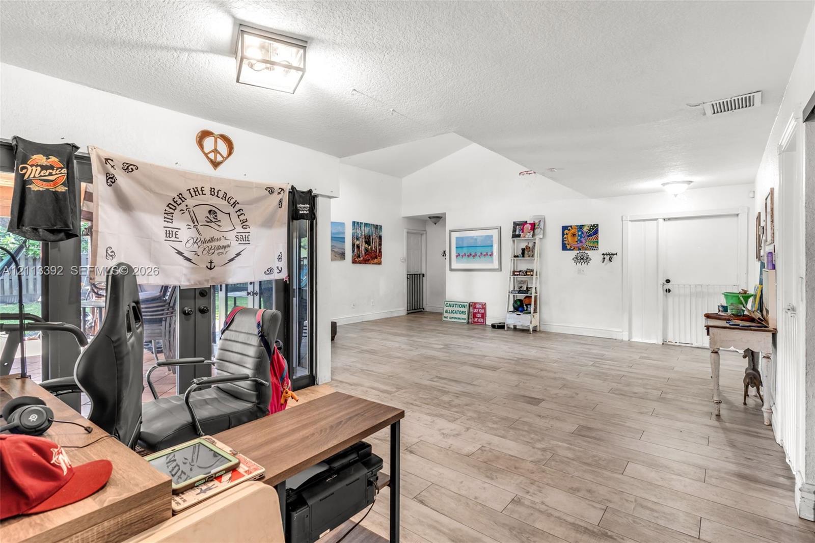 Open floor plan featuring vaulted ceilings, wood-finish flooring, and multi-panel sliding glass doors