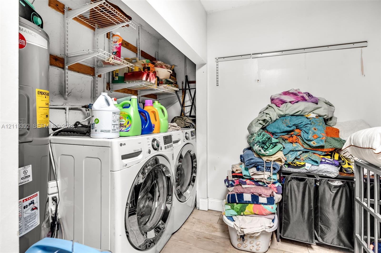 Utility room featuring white front-load laundry appliances, a tall upright water heater, and wall-mounted metal shelving units