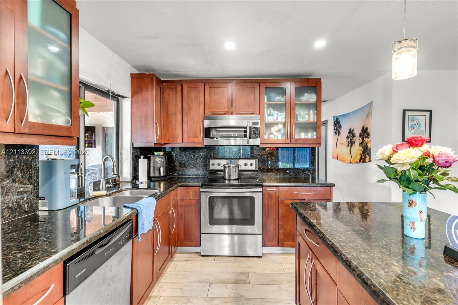Kitchen featuring custom wood cabinetry, dark stone countertops, stainless steel appliances, glass-front upper cabinets, and wood-finish flooring