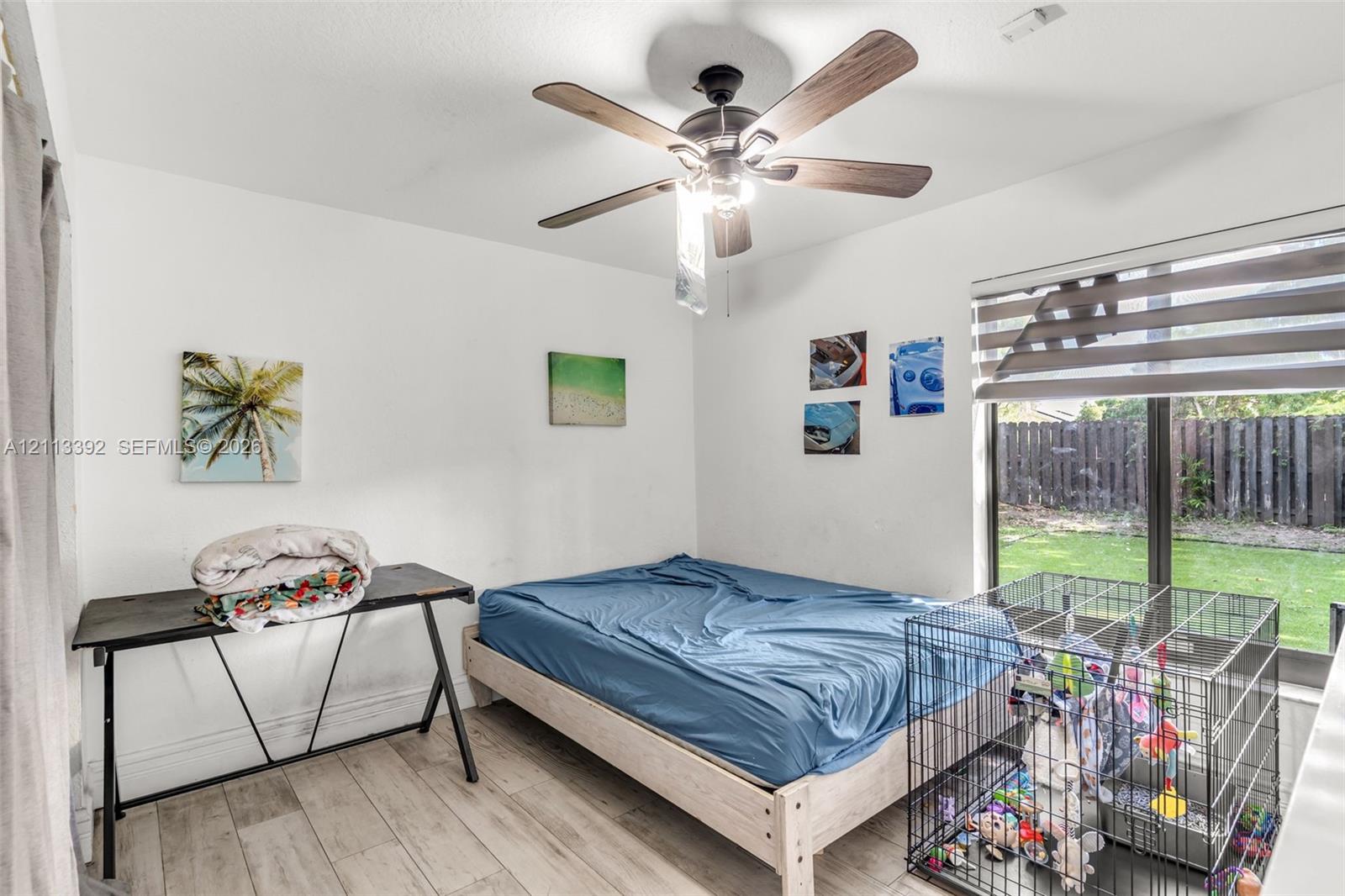 Wood-finish flooring, ceiling fan with integrated lighting, and large window with dual-layer fabric shades