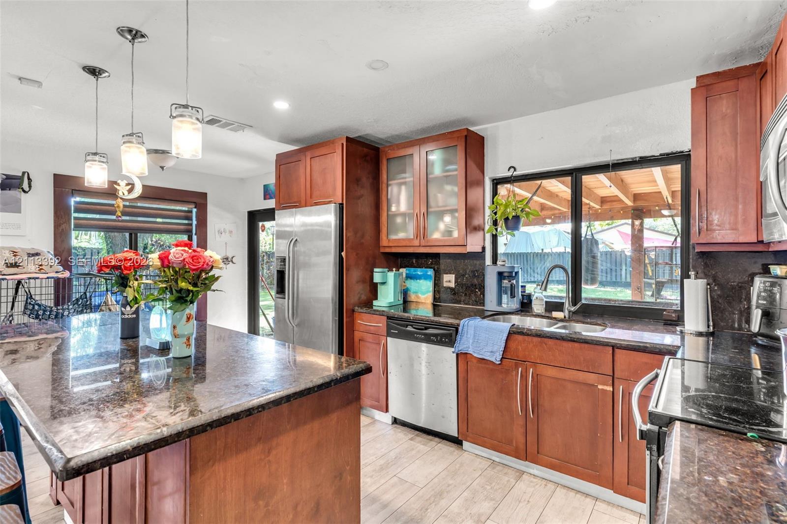 Kitchen featuring a center island, wood-finish cabinetry, stone countertops, stainless steel appliances, and pendant lighting