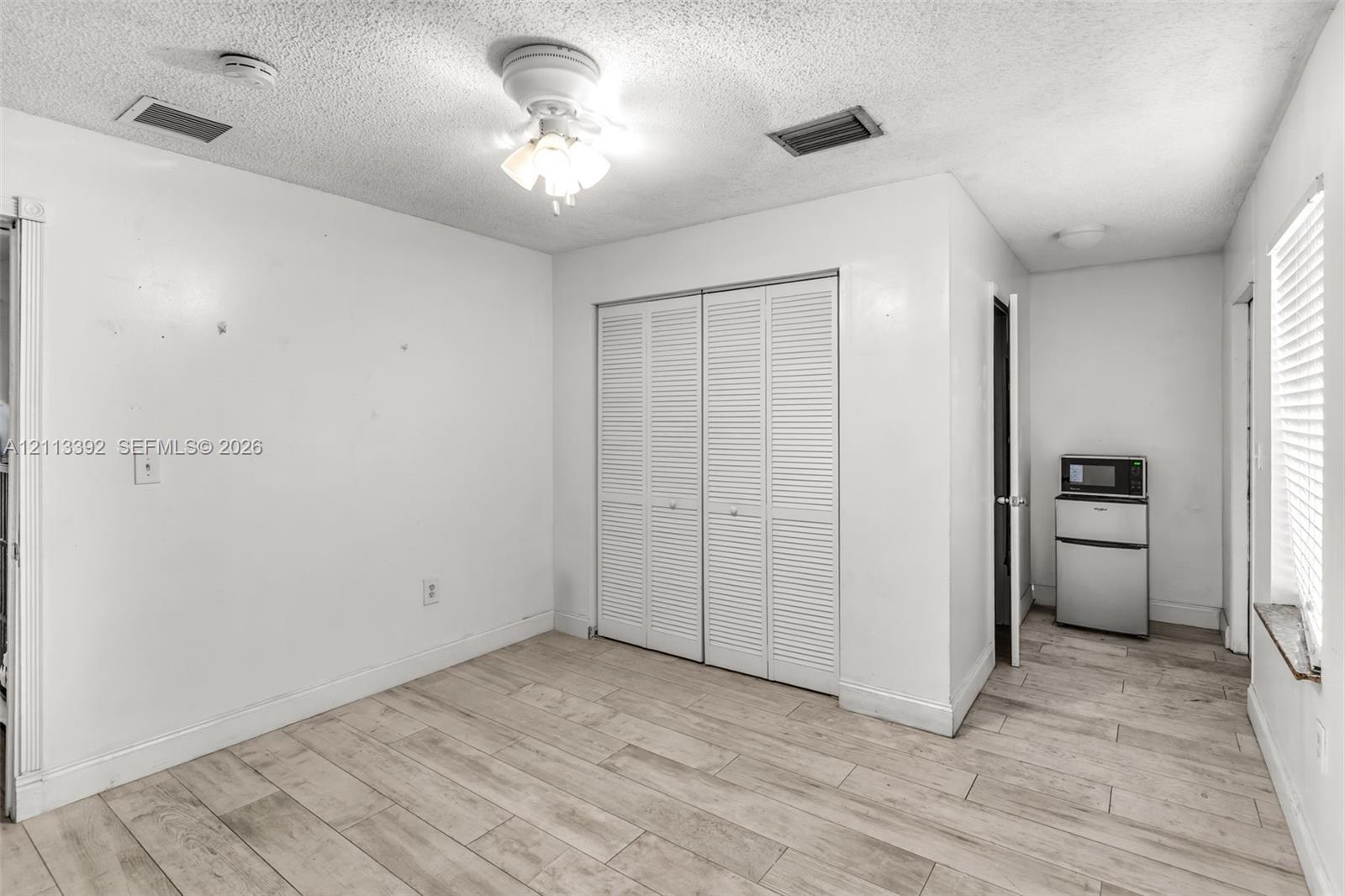 Wood-finish tile flooring, ceiling fan with light fixture, and floor-to-ceiling closet with louvered doors
