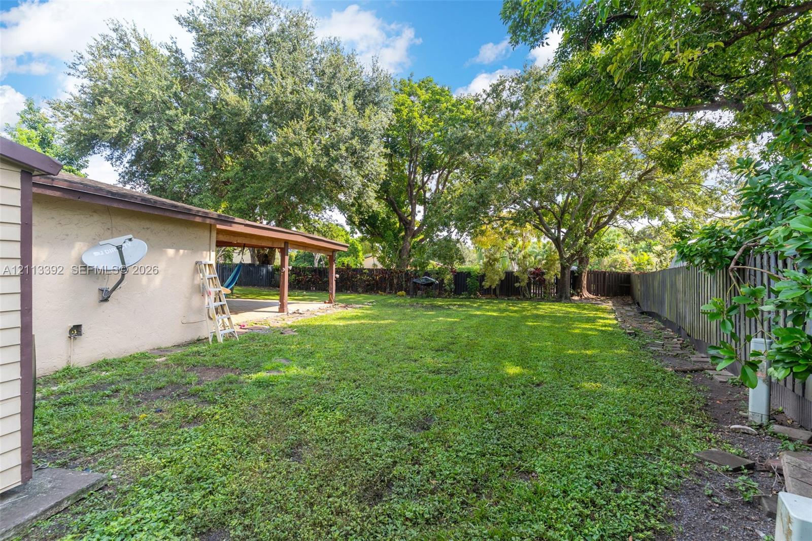 Backyard featuring a covered patio, expansive lawn, mature trees, and wooden perimeter fencing