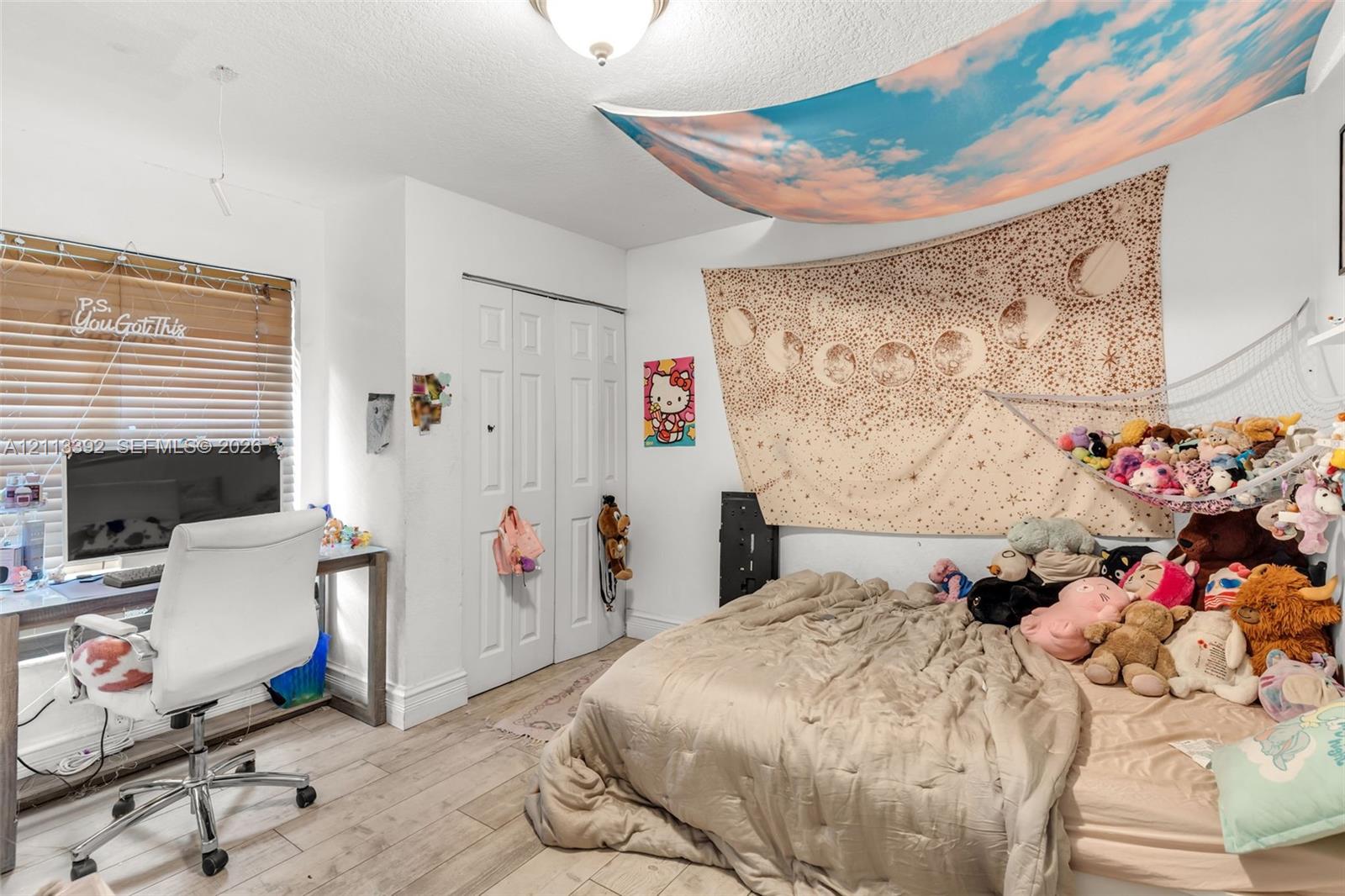 Bedroom featuring wood-finish flooring, white bi-fold closet doors, a ceiling-mounted light fixture, and a large window with horizontal blinds