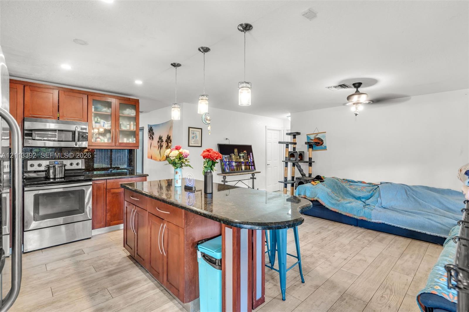 Kitchen featuring wood-finish cabinetry, stone countertops, stainless steel appliances, pendant lighting, and wood-finish flooring