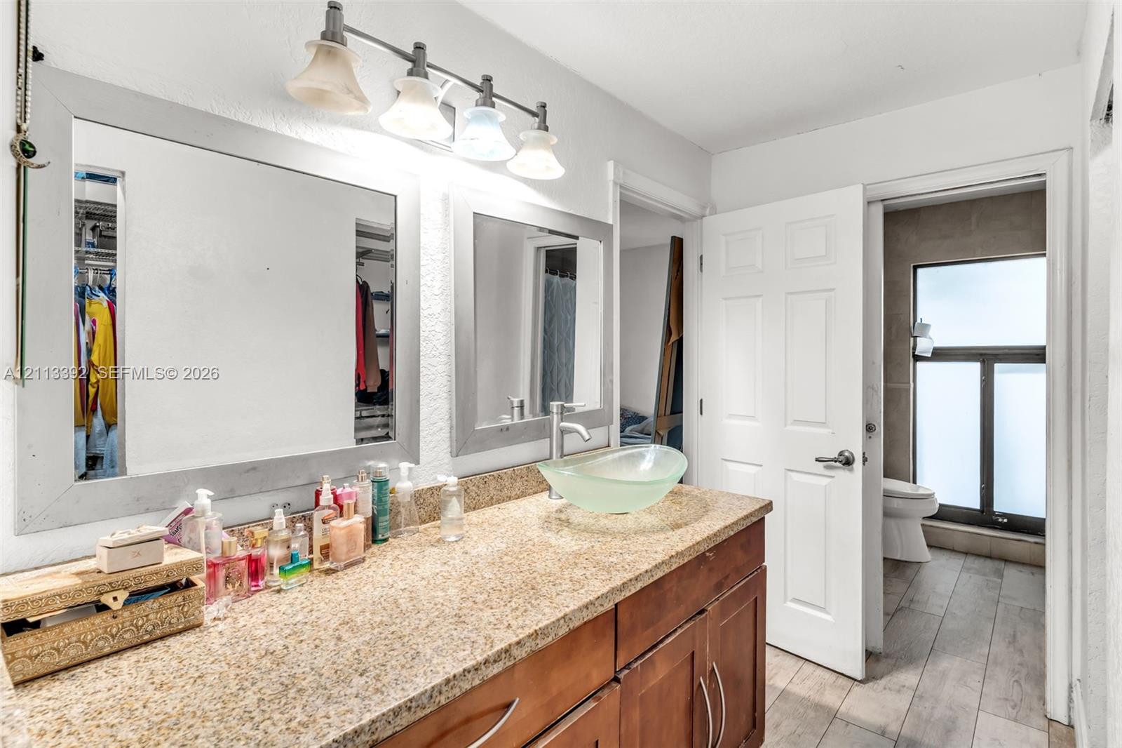 Bathroom vanity featuring a speckled stone-finish countertop, dual wood-tone cabinets, glass vessel sink, and large framed wall mirrors