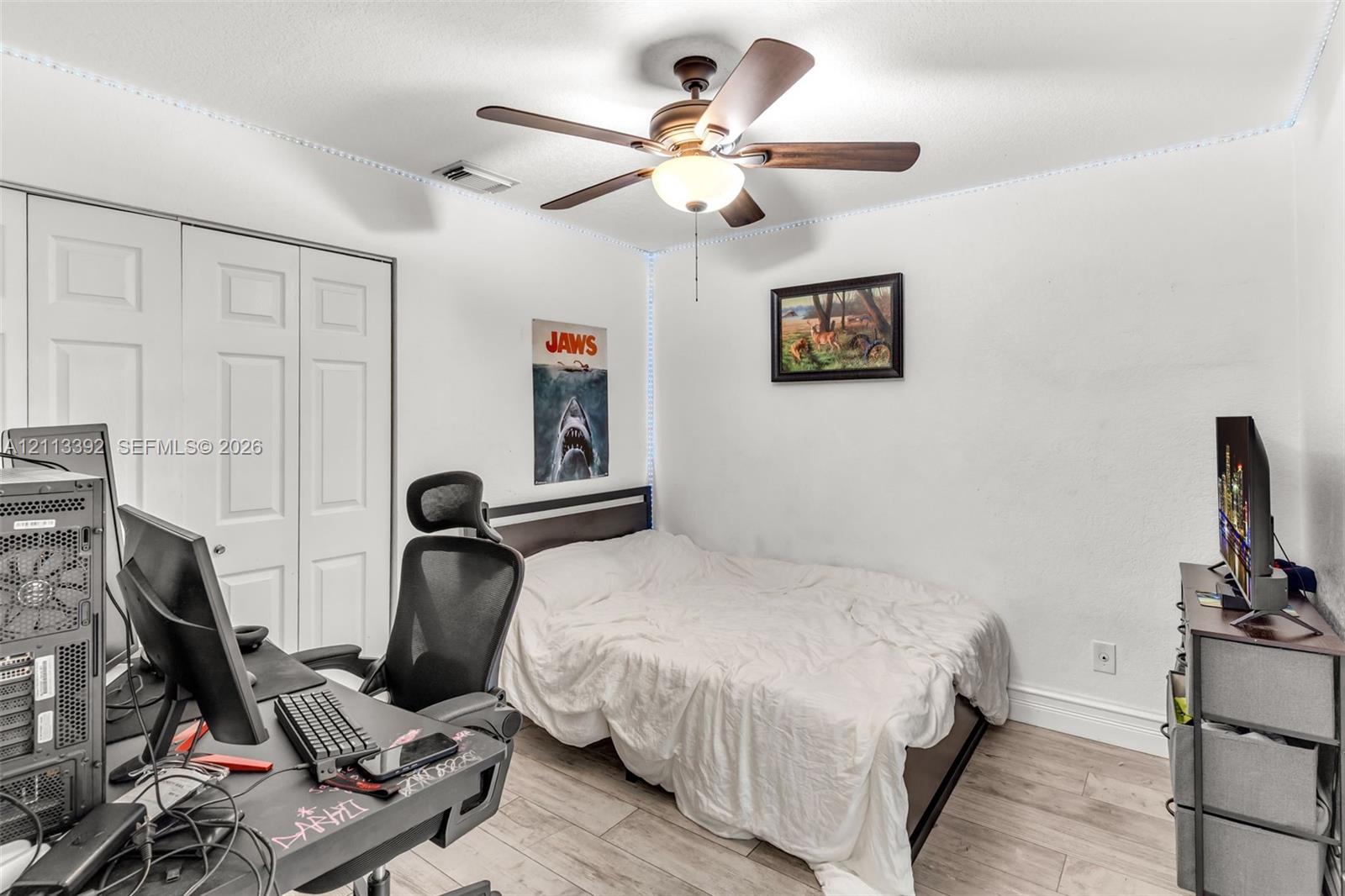 Room featuring wood-finish flooring, ceiling fan with integrated lighting, and dual-panel closet doors