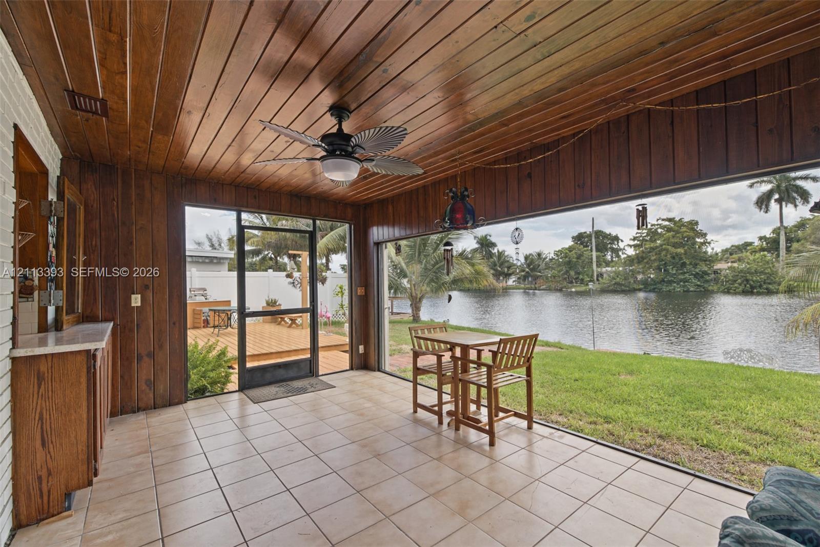 Screened-in porch featuring wood-paneled walls and ceiling, tile flooring, built-in cabinetry, and a ceiling fan
