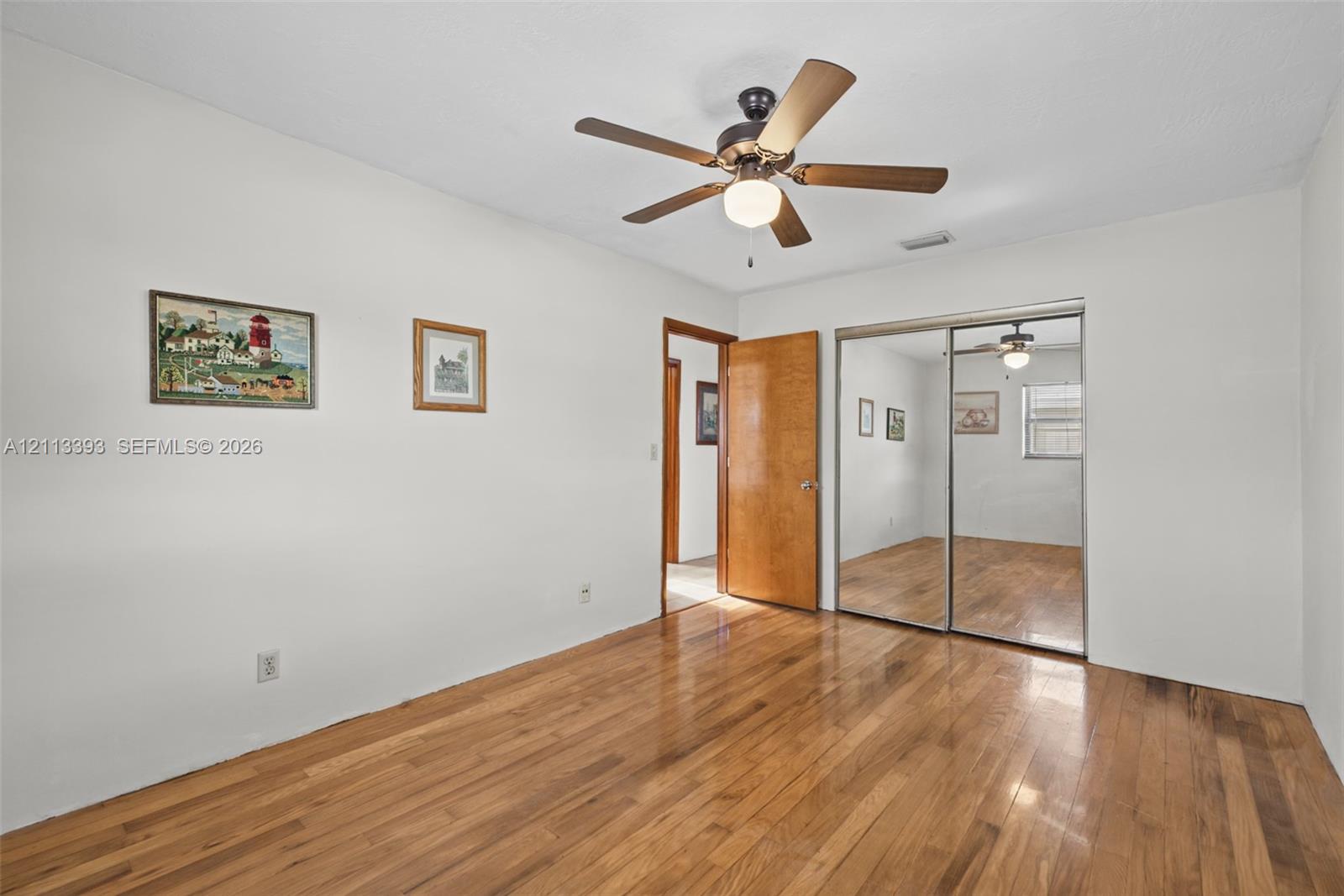 Wood-finish flooring, ceiling fan with integrated lighting, and mirrored sliding-door closet