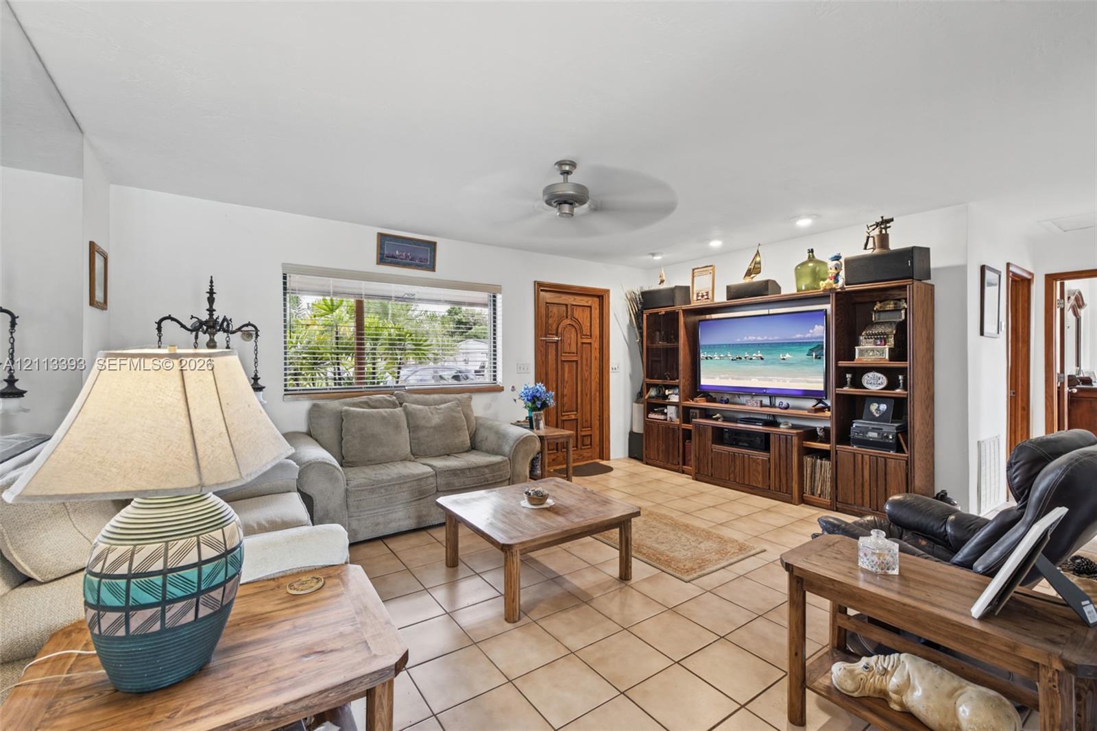 Living area featuring neutral tile flooring, built-in wooden media cabinetry, a solid wood front entry door, and a ceiling fan