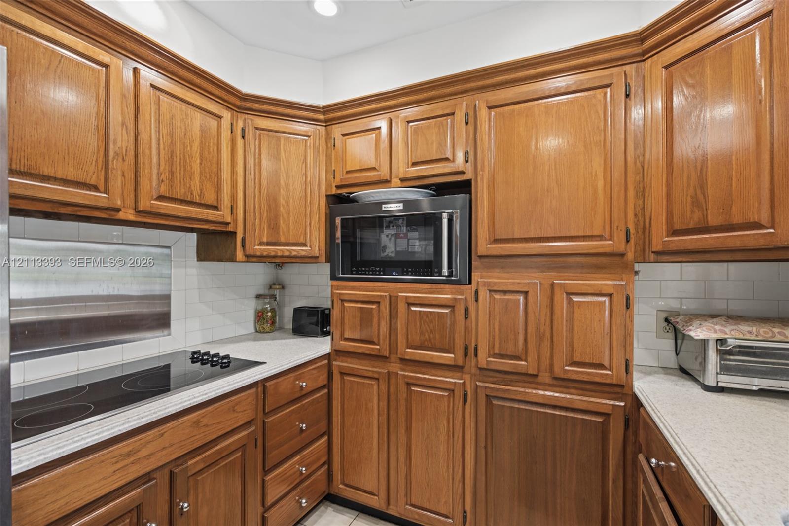 Kitchen featuring natural-finish wood cabinetry, a built-in microwave, a flush-mount electric cooktop, quartz countertops, and a white subway tile backsplash