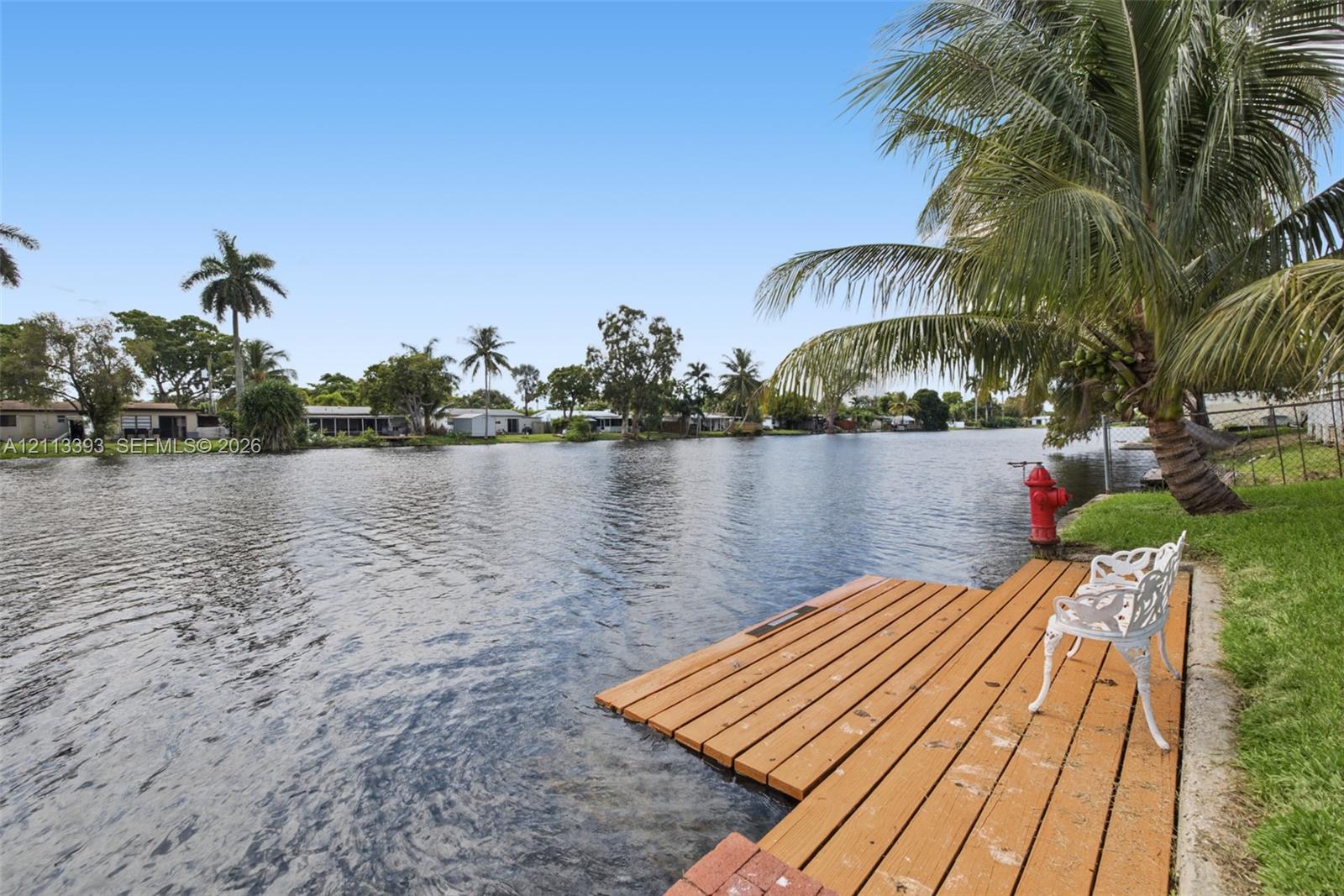 Waterfront property featuring a wood-plank dock, canal access, and mature palm trees