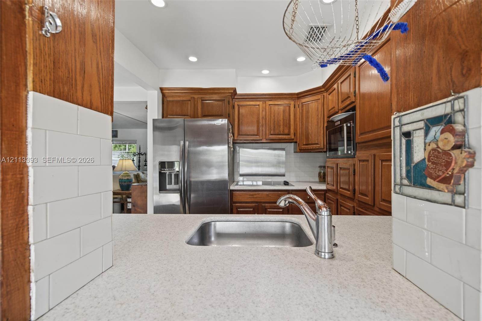 Kitchen featuring recessed lighting, medium-tone wood cabinetry, stainless steel refrigerator, white subway tile backsplash, and quartz countertop with a stainless steel undermount sink