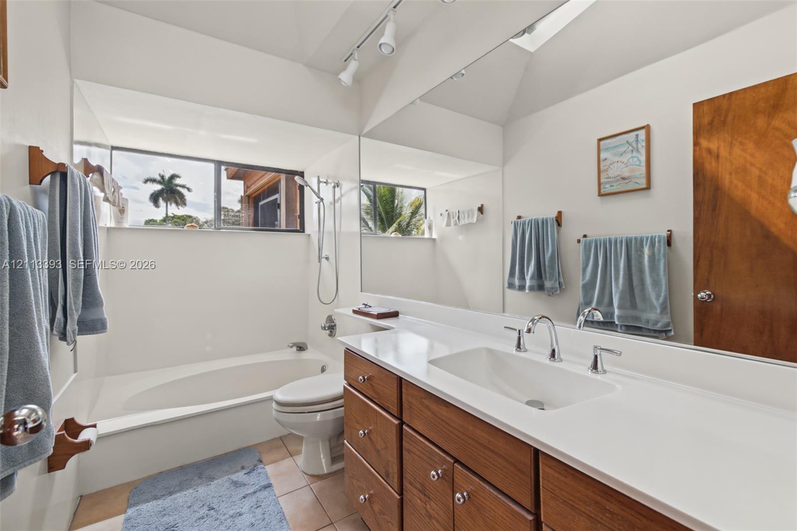Bathroom featuring wood-finish cabinetry, a large wall-to-wall vanity mirror, a rectangular drop-in sink, and a porcelain soaking tub with a handheld shower attachment