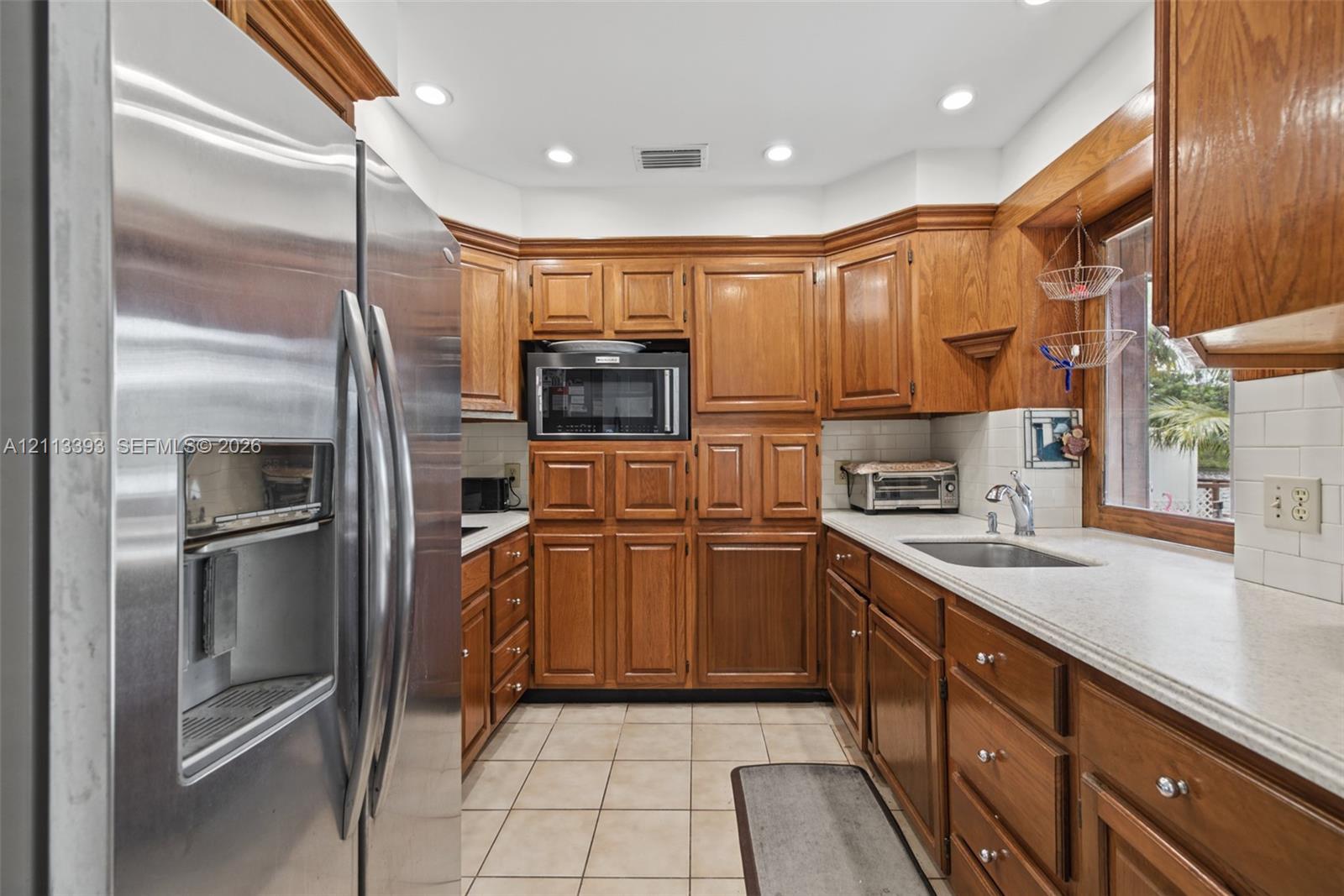 Kitchen featuring custom wood cabinetry, stainless steel refrigerator, built-in microwave, stone-finish countertops, and subway tile backsplash