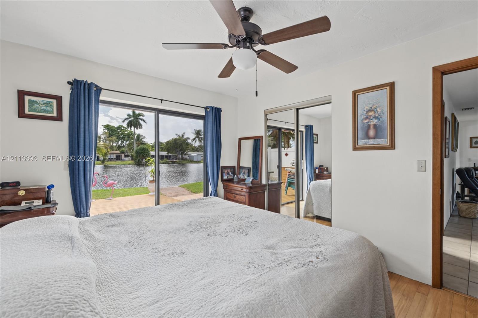 Sliding glass doors, waterfront exposure, wood-finish flooring, and ceiling fan with integrated lighting