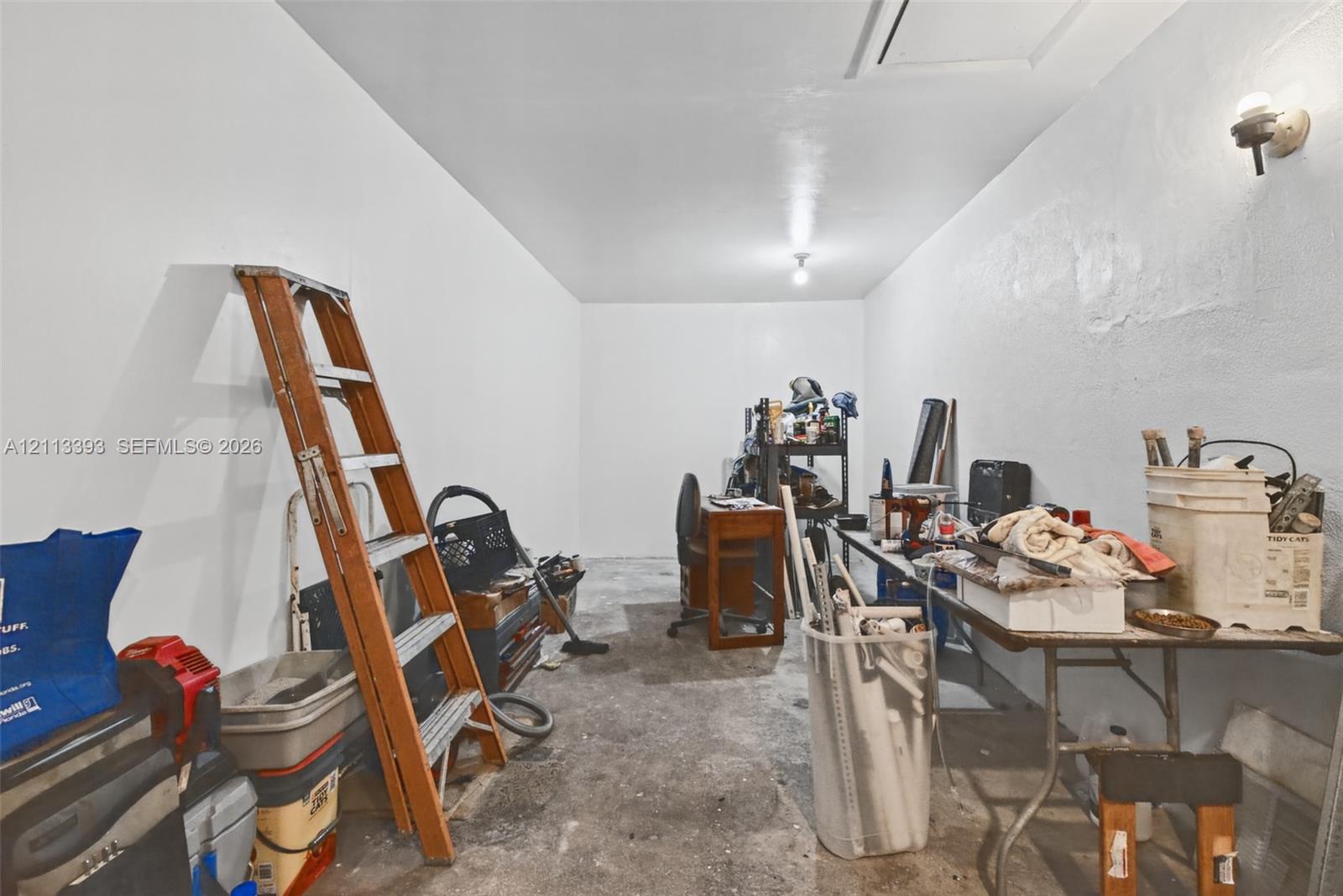 Enclosed storage area featuring white painted walls, a concrete floor, and dual wall-mounted light fixtures