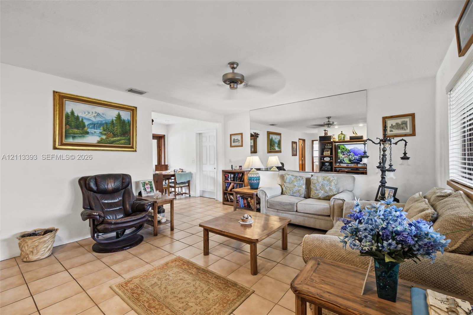 Living area featuring square tile flooring, a ceiling fan, and a large wall-mounted mirror