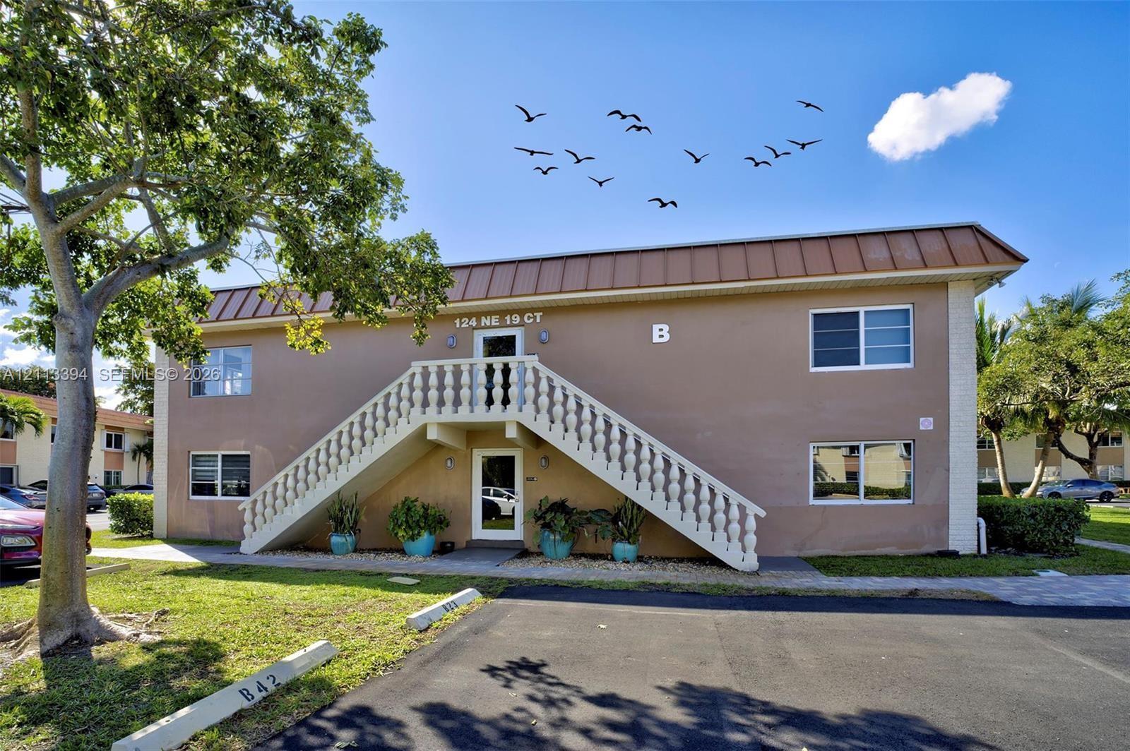 Two-story exterior featuring a metal roof, stucco finish, central staircase with a decorative balustrade, and paved parking