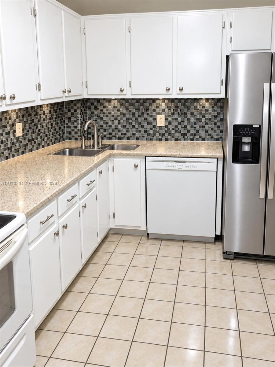 Kitchen featuring white cabinetry, solid-surface countertops, a mosaic tile backsplash, stainless steel refrigerator, and ceramic tile flooring