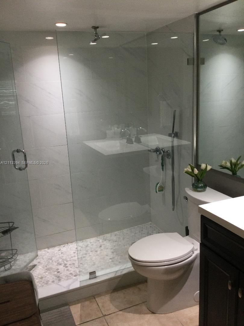 Walk-in shower featuring a frameless glass enclosure, pebble-stone flooring, large-format tile surround, and recessed ceiling lighting