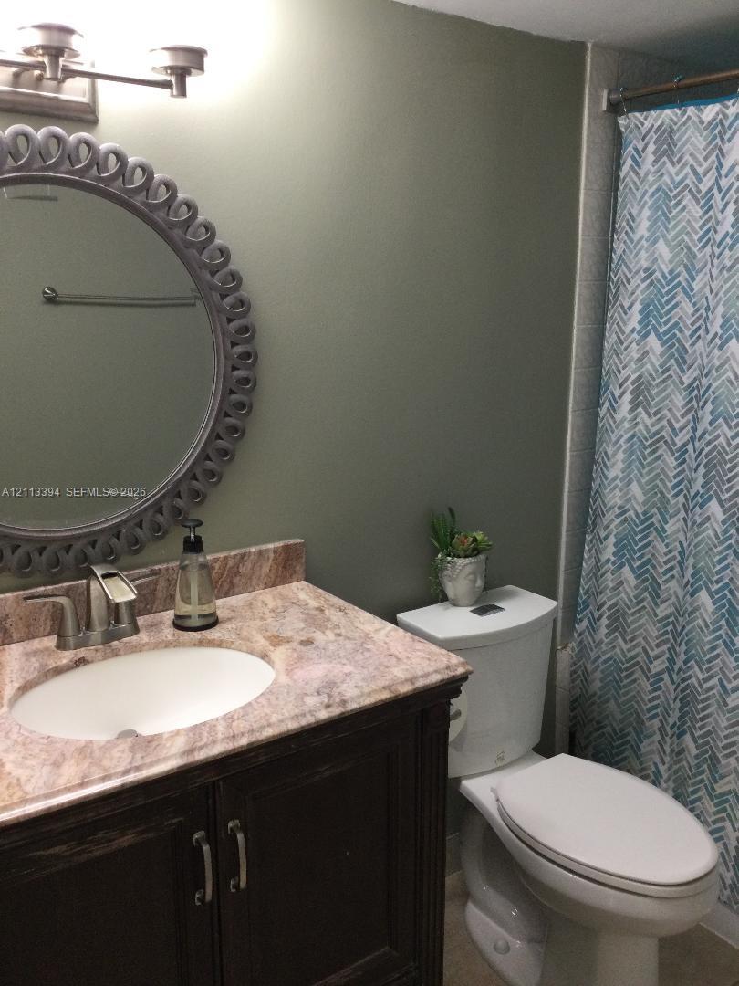 Bathroom featuring a dark wood-finish vanity, stone-patterned countertop, oval under-mount sink, brushed metal faucet, and decorative circular mirror
