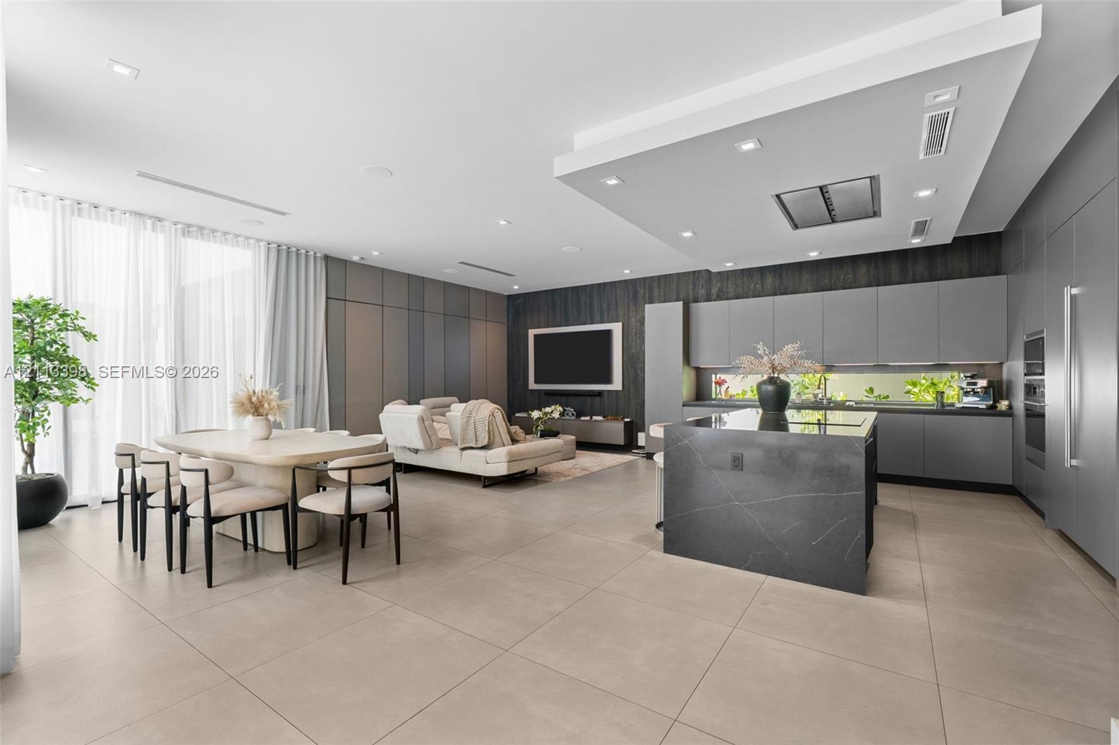 Open-concept interior featuring large-format tile flooring, a kitchen island with stone surfacing, matte-finish cabinetry, recessed ceiling lighting, and a drop-down bulkhead with integrated range hood