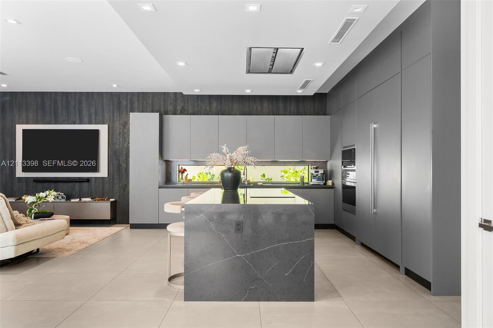 Modern kitchen featuring a central island with a waterfall edge, floor-to-ceiling flat-panel cabinetry, a horizontal ribbon window, integrated built-in appliances, and large-format tile flooring