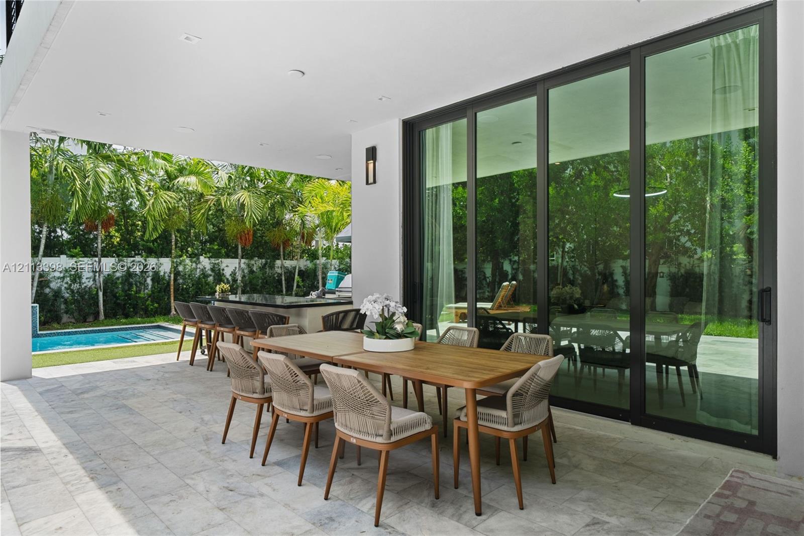 Covered patio featuring stone-tile flooring, floor-to-ceiling glass sliding doors, recessed lighting, and a built-in outdoor kitchen with a stone countertop