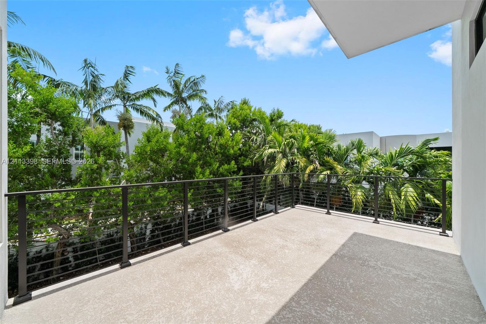Covered balcony featuring concrete flooring, a dark metal cable railing, and dense mature palms