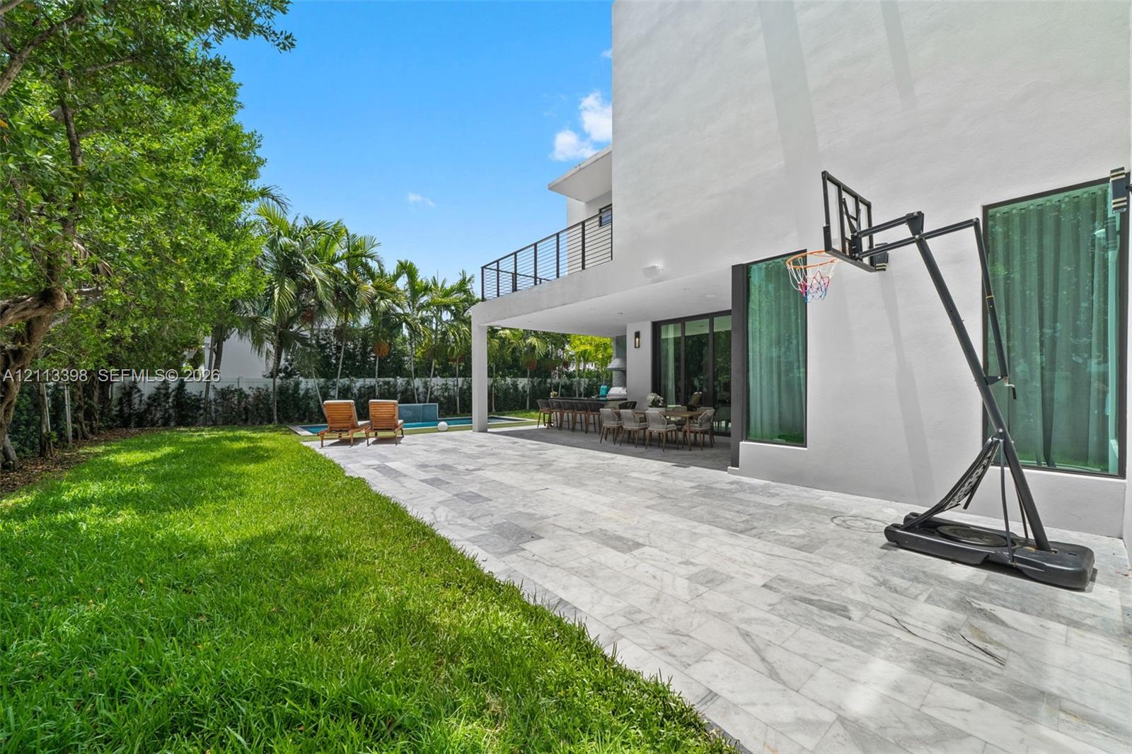 Backyard featuring a paved stone patio, covered terrace, swimming pool, manicured lawn, and second-story balcony with metal railings