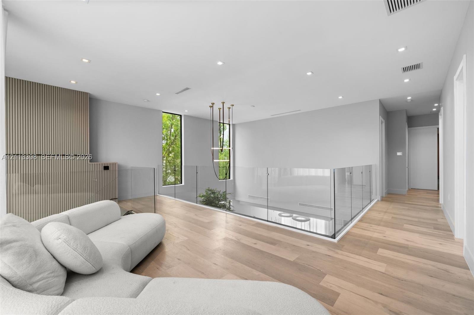 Open-concept space featuring wood-finish flooring, a glass panel railing, vertical wood-slat wall paneling, recessed lighting, and a modern tiered chandelier