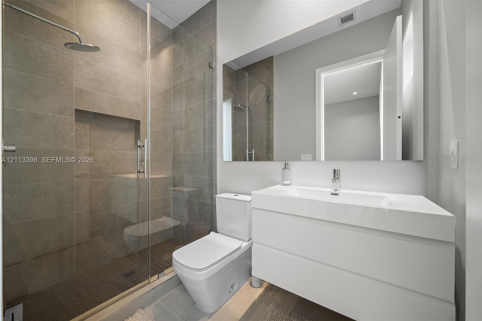 Walk-in shower with floor-to-ceiling tile, rainfall showerhead, and glass enclosure, featuring a white floating vanity with an integrated basin and a large frameless mirror