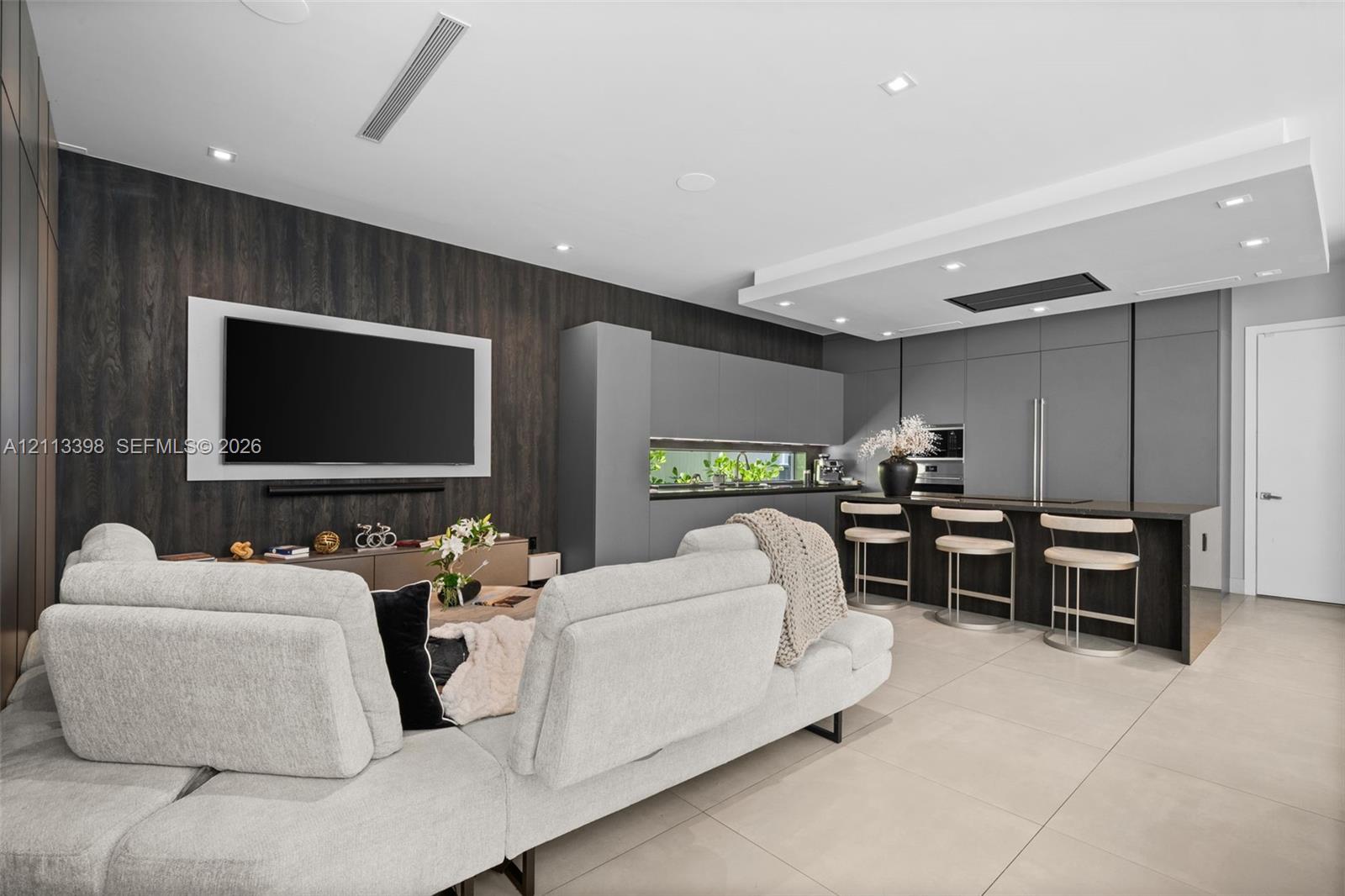 Modern kitchen featuring matte grey flat-panel cabinetry, integrated appliances, a dark wood-finish island with breakfast bar seating, recessed ceiling lighting, and large-format tile flooring